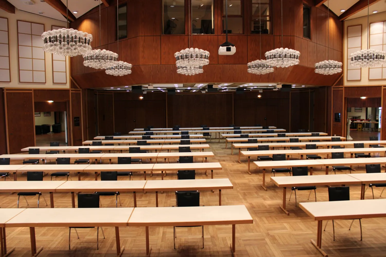 Congress Center Ramstein, leerer Wendelinus-Saal in parlamentarischer Bestuhlung — lange Tischreihen mit Stühlen, Holzvertäfelung und Kugelleuchten über dem Parkett