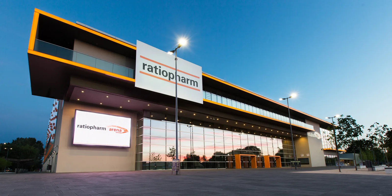 ratiopharm arena Neu-Ulm, beleuchteter Haupteingang in der blauen Stunde